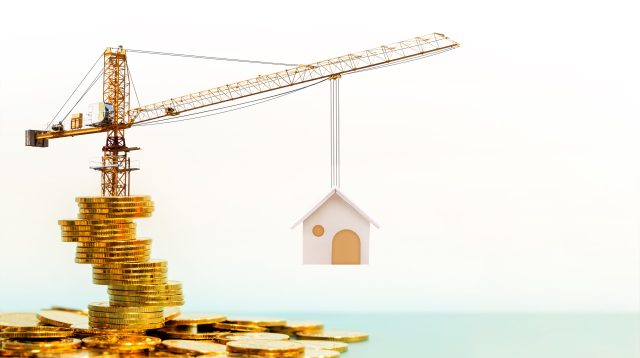 Kran steht auf Goldmünzen und hebt Haus hoch