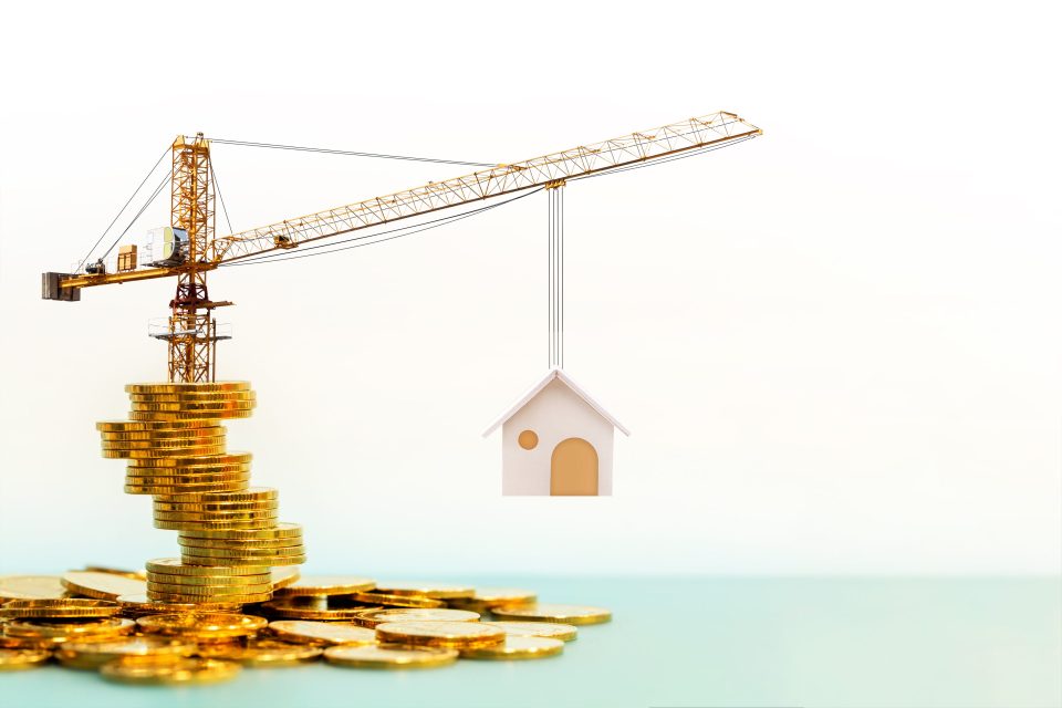 Kran steht auf Goldmünzen und hebt Haus hoch