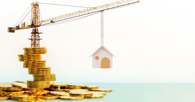 Kran steht auf Goldmünzen und hebt Haus hoch