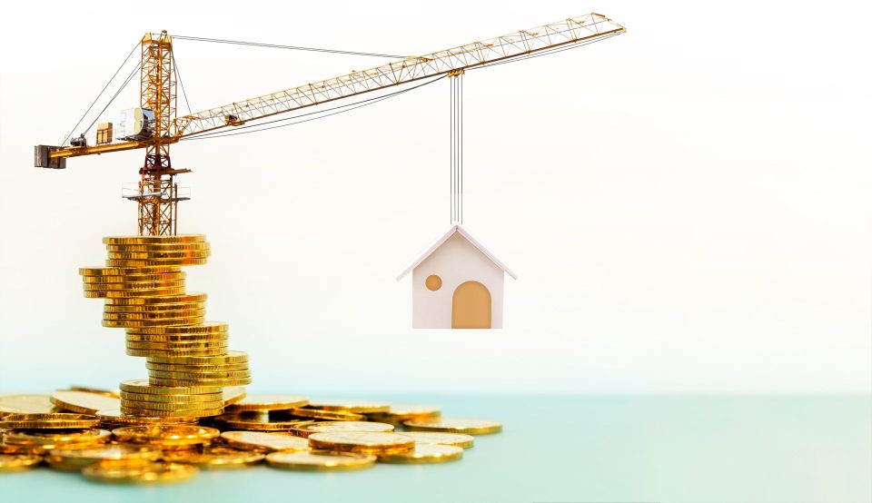 Kran steht auf Goldmünzen und hebt Haus hoch