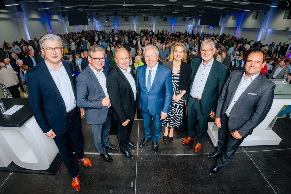 Der frühere WDR-Intendant Tom Buhrow kommt als Gast auf der Mitgliederversammlung der Verbundvolksbank OWL in die Mitte. Bankchef Ansgar Käter steht ganz links. Außerdem im Bild: Paderborns Bürgermeister Michael Dreier, Landrat Christoph Rüther, EU-Parlamentarierin Verena Mertens, Aufsichtsratschef Peter Gödde und Vorstand Thorsten Wolff. Foto: Besim Mazhiqi