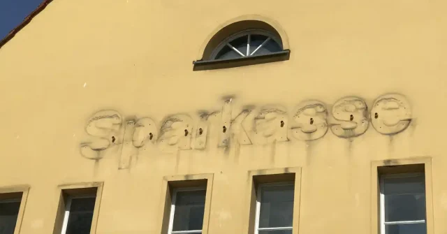 An einer gelben Hauswand wurde der Schriftzug "Sparkasse" entfernt. Die Abdrücke der alten Buchstaben sind noch deutlich zu sehen.