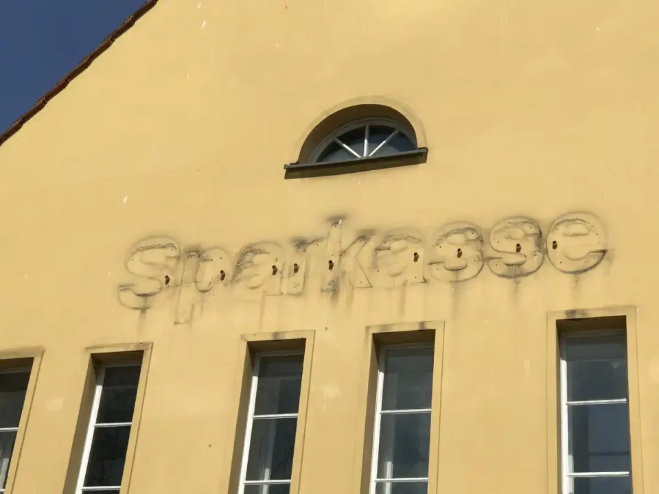 An einer gelben Hauswand wurde der Schriftzug "Sparkasse" entfernt. Die Abdrücke der alten Buchstaben sind noch deutlich zu sehen.