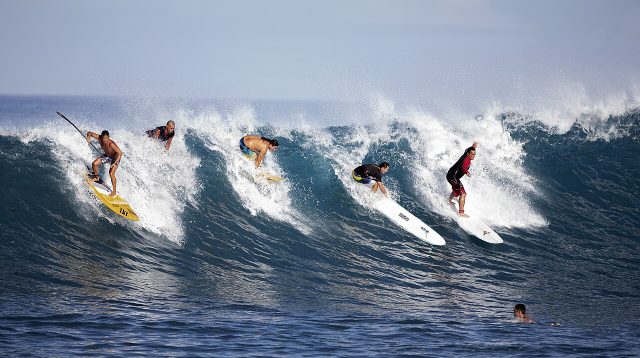 Fünf Surfer, die gleichzeitig auf einer Welle surfen.